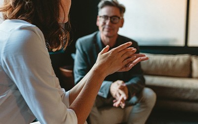 Arms and hands of woman on couch gesturing in conversation with older man blurry in background