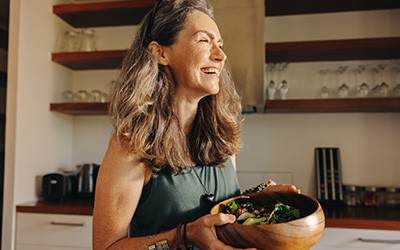 Woman holding wooden bowls with salad in kitchen smiling