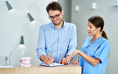 Smiling patient signing forms with dental assistant