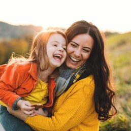 Laughing mother and child sitting in grass on a sunny day