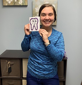 Smiling woman holding a drawing of a tooth in Warsaw dental office