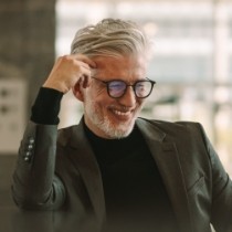 Smiling older man in dark suit jacket resting his head on his hand