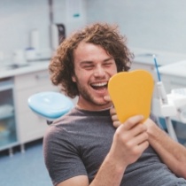 Young man in dental chair seeing his smile in yellow mirror