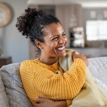 Smiling woman in yellow sweater sitting on couch