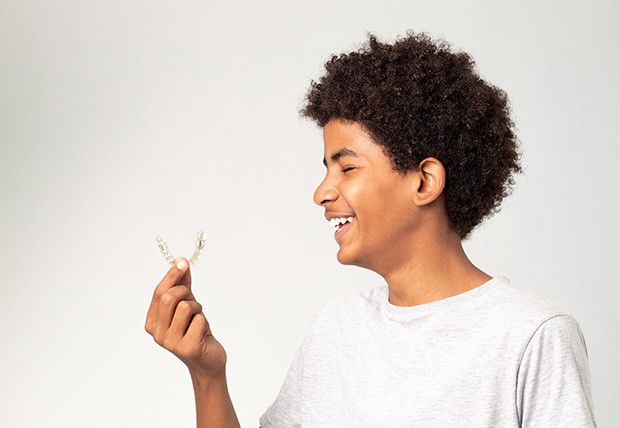 Teenager smiling while holding clear aligner