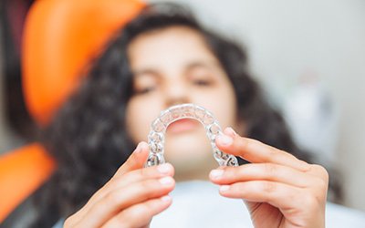 Teenage girl smiling while holding aligner in treatment chair