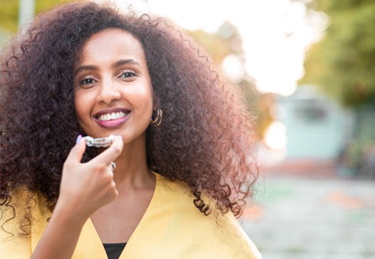 Woman in yellow shirt smiling while holding clear aligner