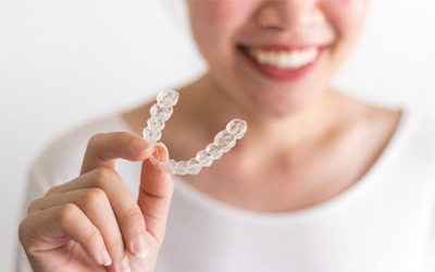 Closeup of smiling woman holding clear aligner