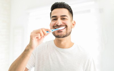 A smiling man brushing his teeth