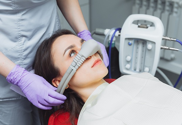 Dentist in purple gloves placing nitrous oxide mask over patient’s nose