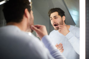 person looking at their mouth in a bathroom mirror