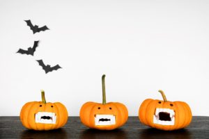 3 small jack-o-lanterns with fake vampire teeth with 3 paper bats on the wall