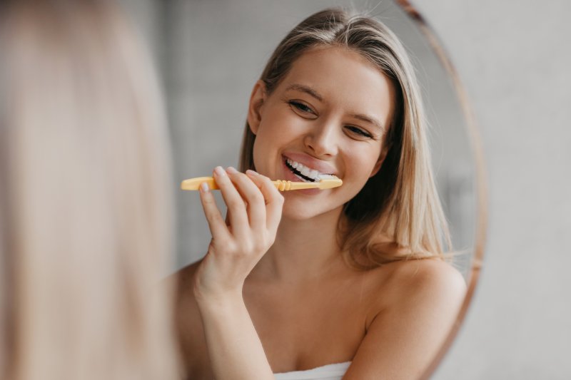 A woman brushing her teeth in front of a bathroom mirror